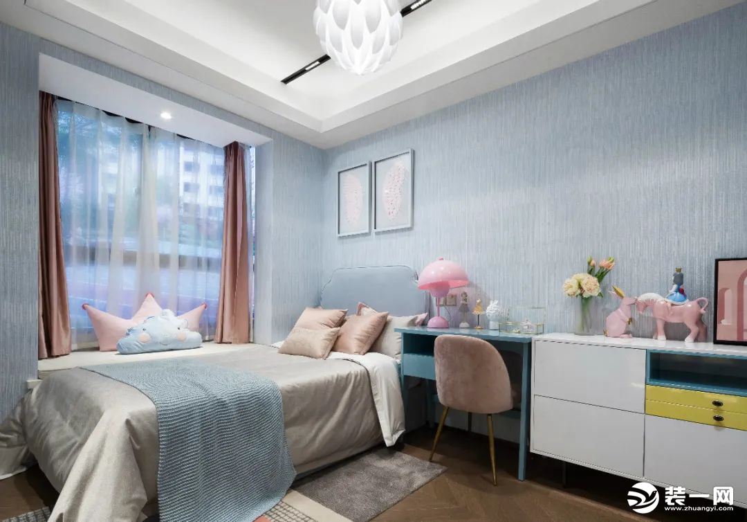 儿童房的墙面贴上蓝色带浅竖纹的墙布基础，靠飘窗布置床铺，右侧是书桌+矮柜的组合，布置粉色抱枕枕头与小
