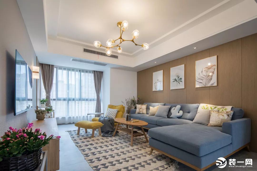 客厅以暖色为主，背景墙一面灰色，一面木色，大气又不失清新之感。蓝色的布艺沙发，黄色的休闲躺椅，让家里