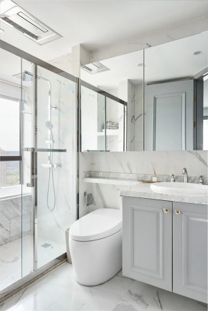 卫生间的雅白地面与墙面砖，结合淡灰色的浴室柜，洗手盆与马桶后方装上镜柜收纳，洗手台的台面延伸到马桶后