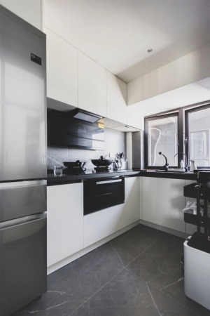 厨房，经典的黑白灰搭配，看上去简洁时尚。采用了L型的橱柜布局，并将冰箱嵌入进去，空间的极致利用。