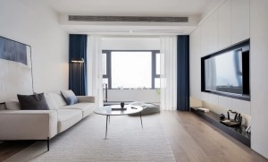 客厅，将阳台隔墙打通，改用蓝白色窗帘代替，解决了采光不佳的问题。地面通铺木地板，搭配舒适的米色布艺沙