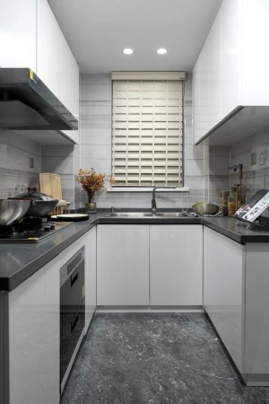 厨房在深灰色地砖的空间基础，厨房操作台也是以灰色的材质，结合白色橱柜与吊柜，窗户装着百叶帘，现代优雅