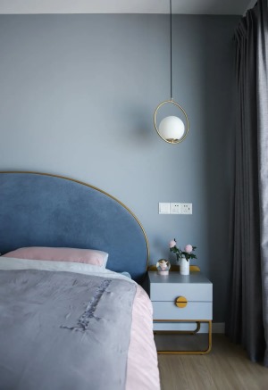  卧室在蓝色的床头背景墙的墙面基础，两侧加入球形壁灯与吊灯，布置一张灰蓝色的布艺靠背的金属架床铺，整