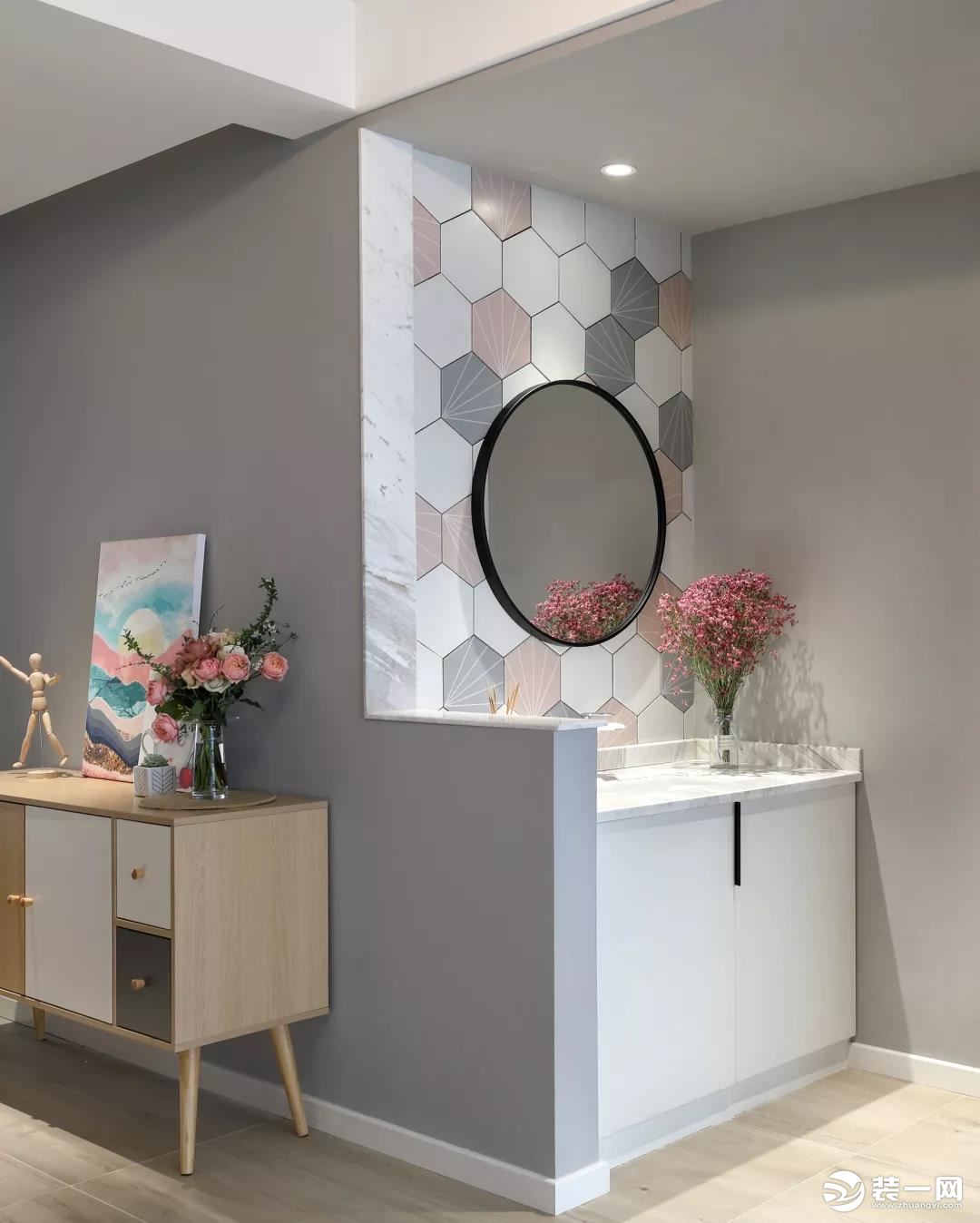 公卫的洗手盆设置在过道区域，以矮墙为隔断，墙面在灰白粉色的六边砖搭配下，挂上一面圆形的黑框镜子，布置