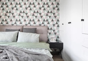 卧室床头墙贴着三角图案的墙布，图案里的三角形以黑白粉青多种颜色交替，布置灰色靠窗的床铺，简洁素雅的床