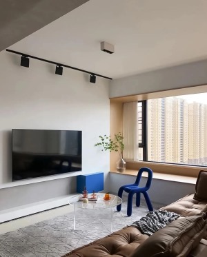 电视背景墙利用灰白蓝三种颜色进行色块组合，墙面的表现形式简练而富有艺术气息，原有灯带替换成轨道射灯，