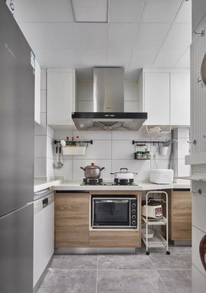 精致的小厨房，巧妙地把各类电器嵌入到橱柜里，还放了一个移动式的料理架，在灰色地砖、白色墙砖与木质橱柜