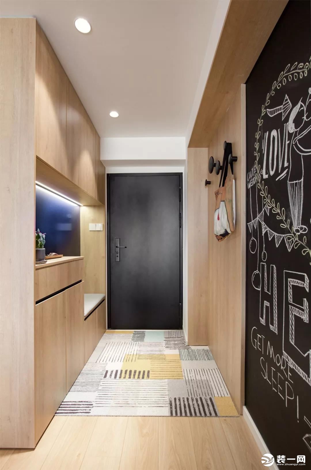 玄关的黑色大门与里面的黑板墙相呼应，整体木色的定制柜与护墙板，地面的线条纹理地毯，则是让空间更加清新