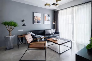 客厅以水泥灰质感的地砖，搭配灰色调的墙面，布置上黑色皮沙发，还有橙色沙发椅，营造出一个简约舒适而有活
