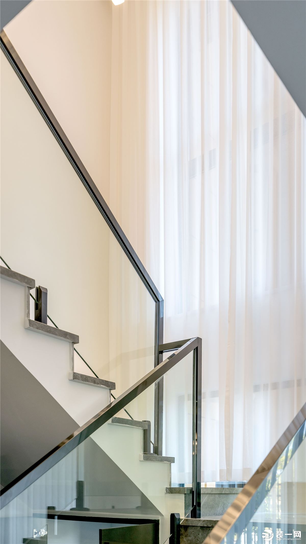 楼梯的护栏采用了玻璃的材质配上钛黑色的不锈钢扶手，再搭配上亮灰色的大理石瓷砖，整体非常的显高级、清冷