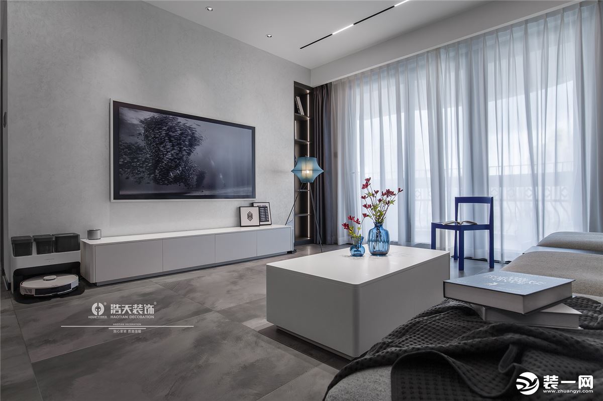 客厅的装饰以灰白色为主，辅以沉稳的蓝色，再加上落地灯以及各材质营造出的质感，整体的布局简洁大气。