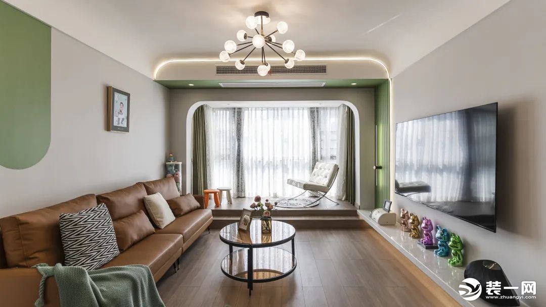 客厅，在以灰绿构建的空间内，焦糖色沙发的加入，混搭却不突兀。地面以温润的木地板通铺，连通阳台，阳光穿
