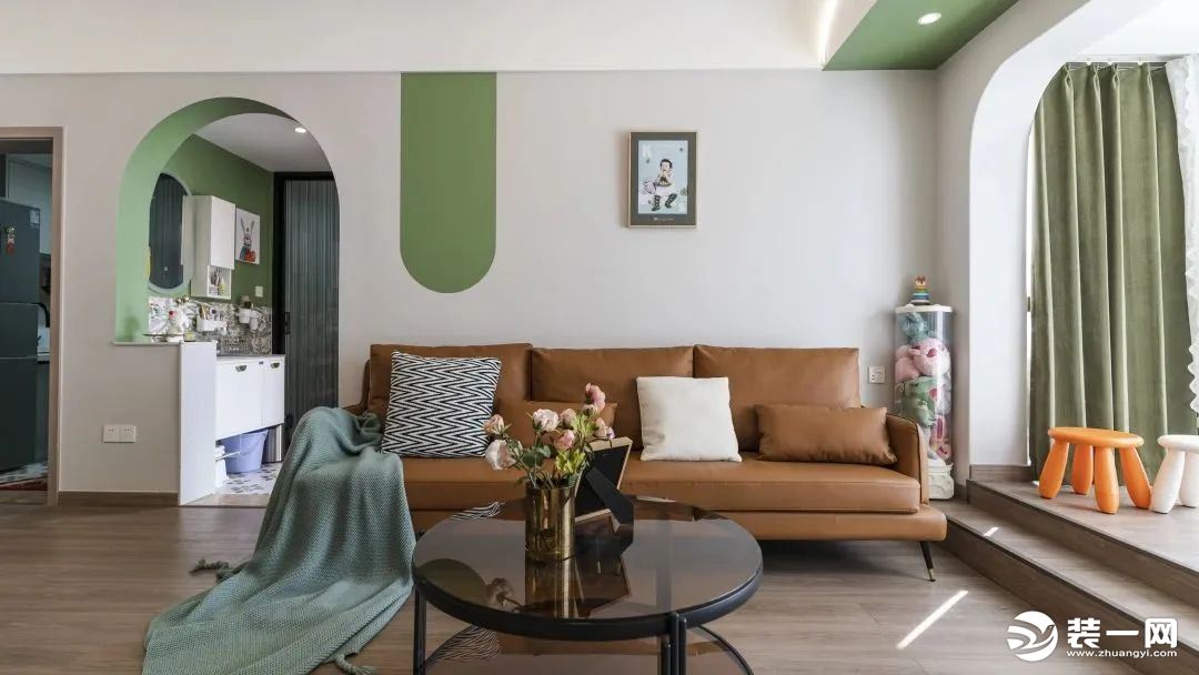 沙发背景墙局部也做了绿色乳胶漆，散发着春日的暖意。时尚又精致的焦糖色沙发，搭配茶色圆几，陈设简洁大方