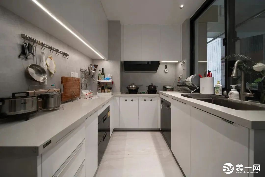 中厨区以U字形的操作台设计，净白的橱柜与吊柜，加上灰色的操作台，墙面加入实用的挂钩，厨具整齐收纳，让
