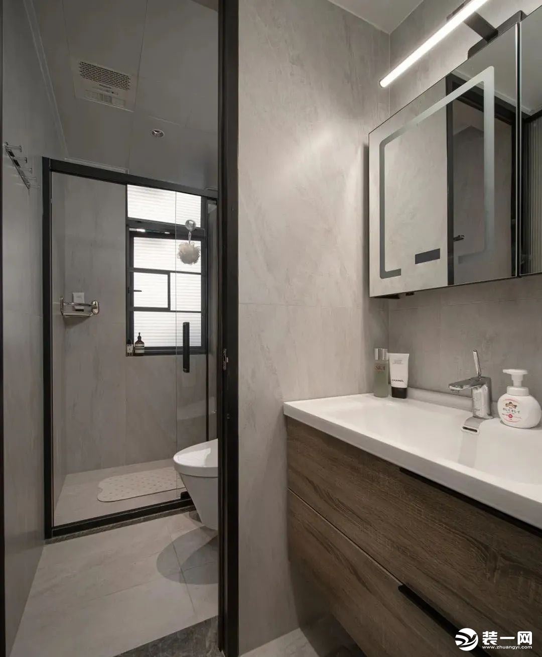 卫生间，选择半隔断的设计进行干湿分离，定制深色实木浴室柜，镜柜上方安置线性灯带，淋浴间以玻璃移门相隔