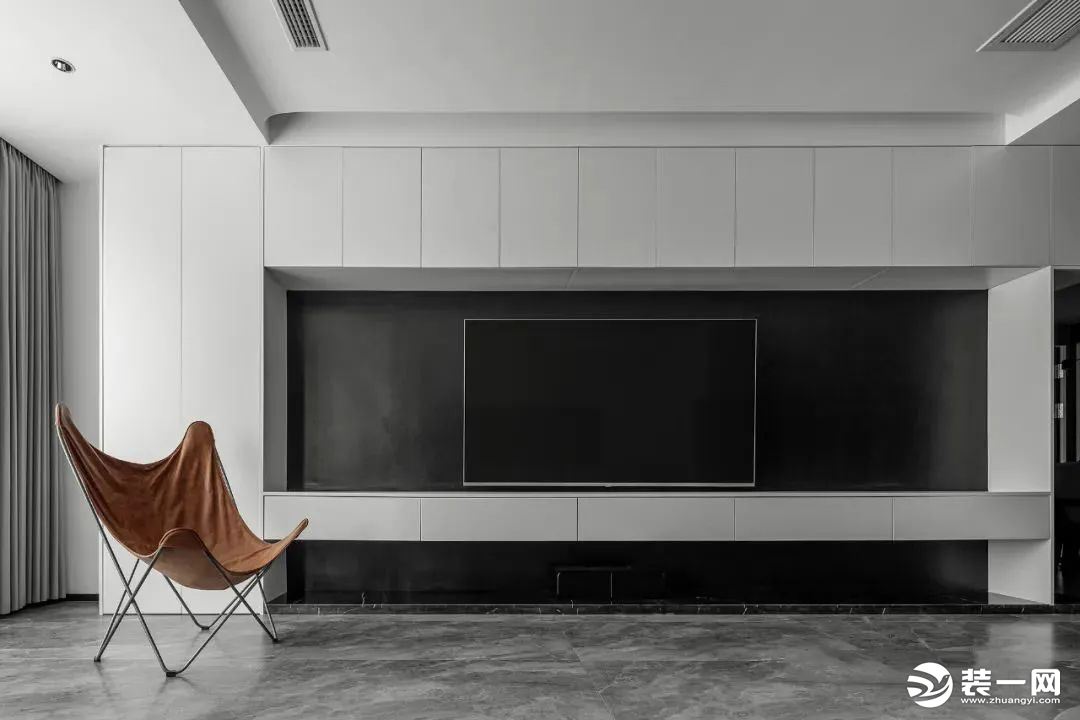 定制“收纳电视墙”，大面积设计白色储物柜，中间部分以纯黑做背景饰面嵌入电视机，底部抬高悬空形成地台，