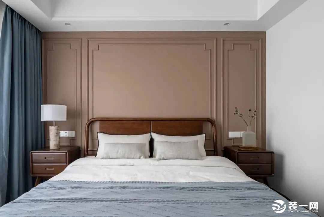 床头背景选择奶咖色艺术漆，两侧布置对称胡桃木床头柜，家具简单而质感，沉稳的木色平衡了空间的暖色调，达