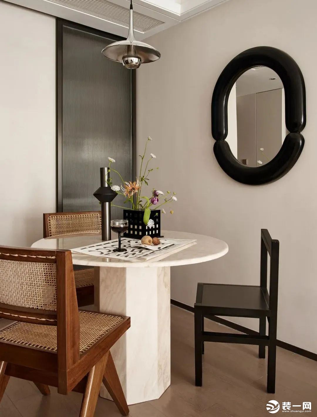 布置奶白色艺术圆桌，搭配藤编元素的餐椅，上方以一盏电镀银的飞碟款吊灯点缀，墙面以墨色圆镜勾勒单调的背