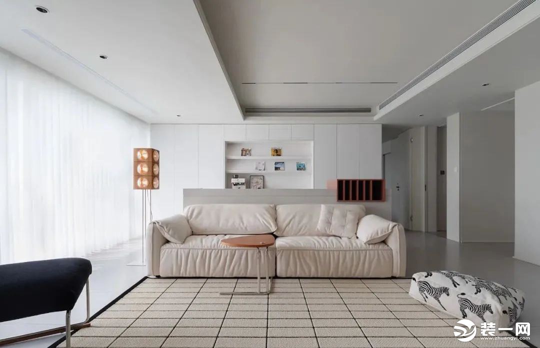 居中摆放一套休闲的布艺沙发，搭配浅色格纹地毯划分空间，取消传统茶几布局，改以小巧的边几置物，留出充足