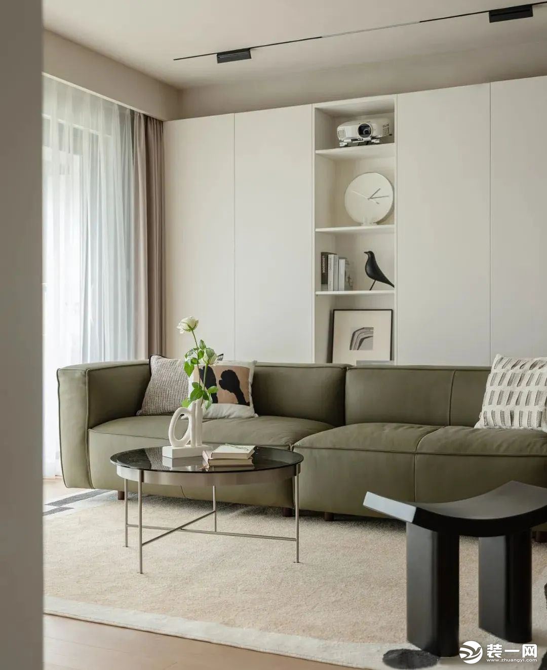 选择一款灰绿绒布材质的沙发，为空间注入复古格调，浅色地毯与背景整体拉开空间感，搭配镜面茶几与创意矮凳