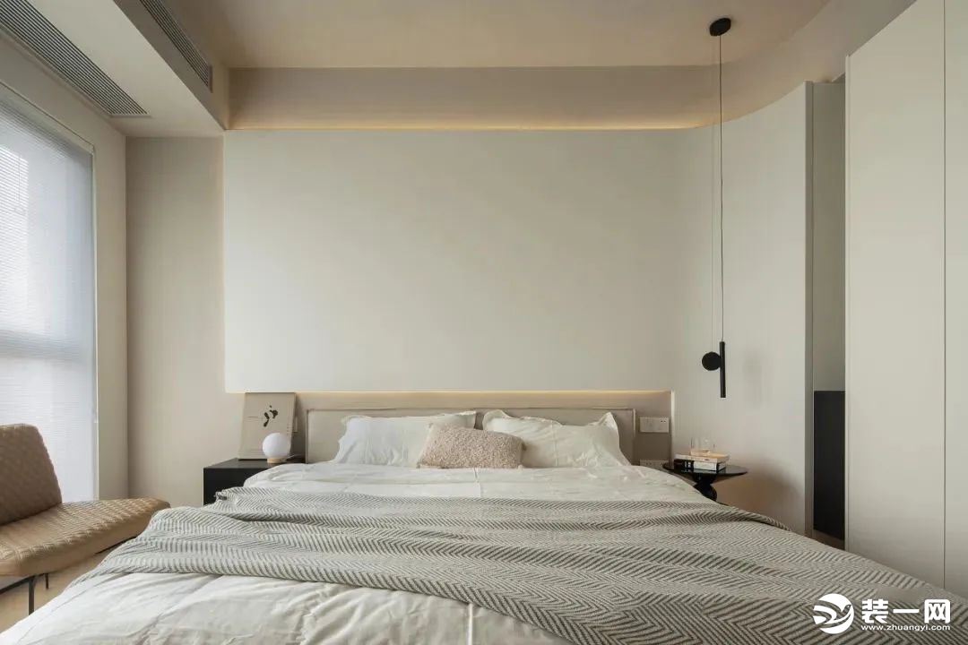 床头背景设计凸出奶白色体块造型，周围嵌入灯带营造温馨的氛围光源，搭配一盏极简线型吊灯，空间柔和唯美的