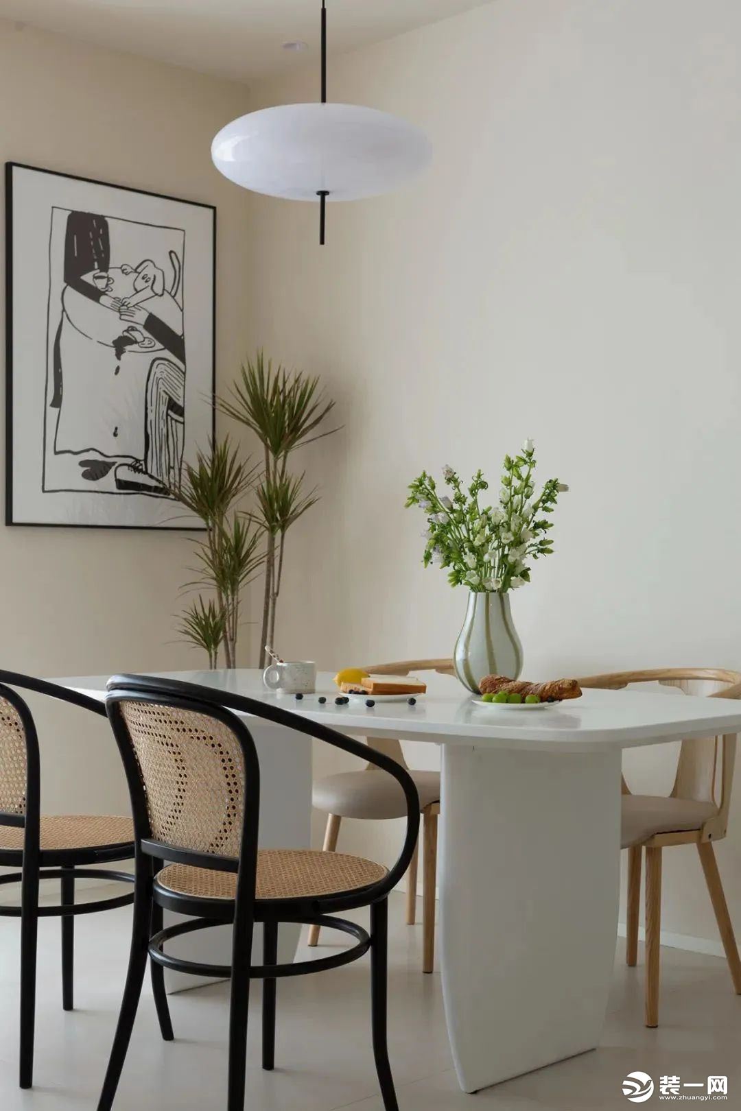 布置纯白色餐桌搭配不同款式餐椅，餐桌圆润的弧线勾勒柔和空间，藤编元素的融入更显自然温馨，现代的吊灯与