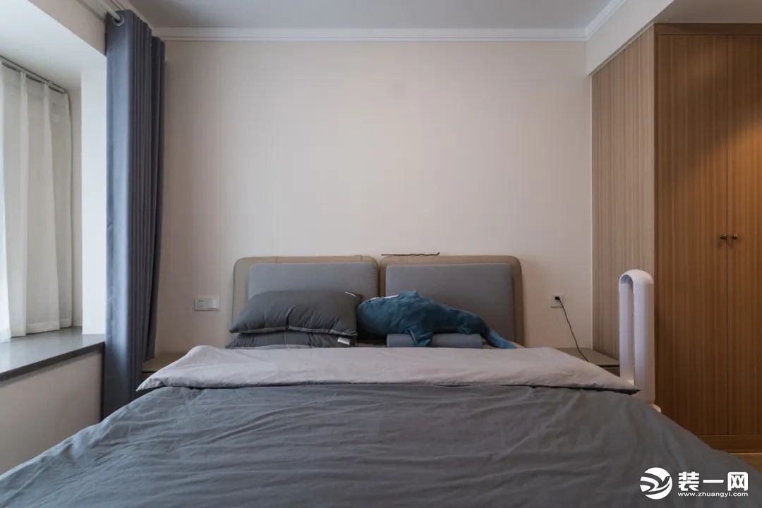 灰蓝色软包床头+同色系床品，搭配简约留白的背景墙，搭建一方悠闲惬意的居所。原木色衣柜，一门到顶，充分