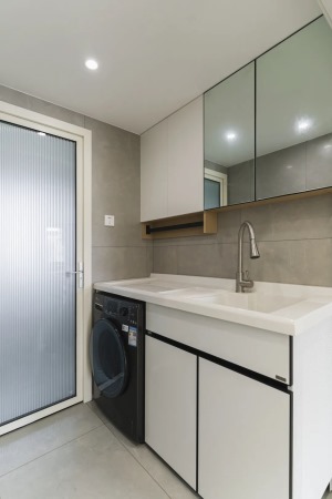 卫浴柜旁安置小型嵌入式洗衣机，空间最大化利用。上方白色吊柜与镜柜并排。顶面极简的无主灯布局，简洁不显