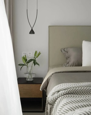 一侧摆置实木床头柜，底部镂空设计，一盏线性吊灯做装饰兼具照明，搭配绿植点缀空间，烘托温馨舒适的睡眠氛