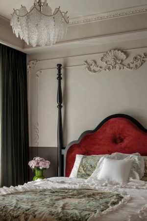 床头一角，床头背景半墙设计，精美的花纹勾勒点缀，以红色强调视觉聚点，搭配水晶吊灯传达法式特有的内敛与