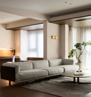 简约舒适的空间下，以浅灰色布艺沙发，搭配深灰色地毯与质感的圆形茶几，角落的大型绿植点缀