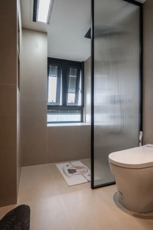衛生間淋浴房做了下沉式處理，單扇玻璃固定，不做推拉門，倒顯得空間尤為寬敞，米灰色瓷磚的質感又增加幾分