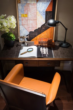 书房位置的设计更显复古韵味，深色调的书桌台灯、橙色的皮面座椅、个性的装饰画与绿植点缀