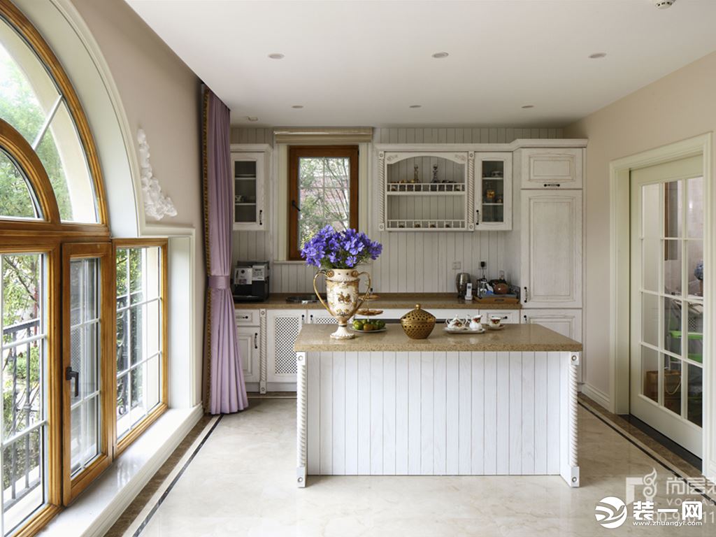 开放式的厨房有个独特的弧形窗户设计，爵士白色的柜子和中岛台的颜色相一致
