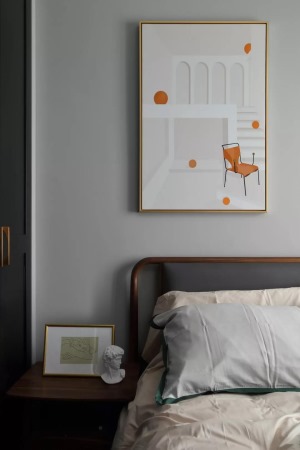 ▲床头墙的空间画面装饰画，画面上的是简洁的空间与橙色椅子、小点，结合床头柜的装饰画与头像摆饰，显得更