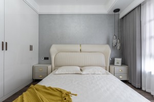 灰白系的卧室基调，暖心而雅致。 米白色的床与床品，搭配金边的床头柜、灰色的窗帘、粉蓝色系的大海装饰画