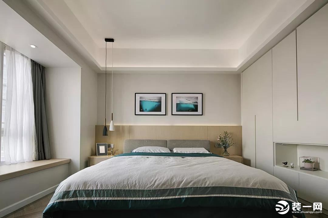 卧室的床头背景墙墙角部分是木色护墙板，上部分的墙面挂上2幅装饰画，情调的飘窗，衣柜中间留空出一个作为