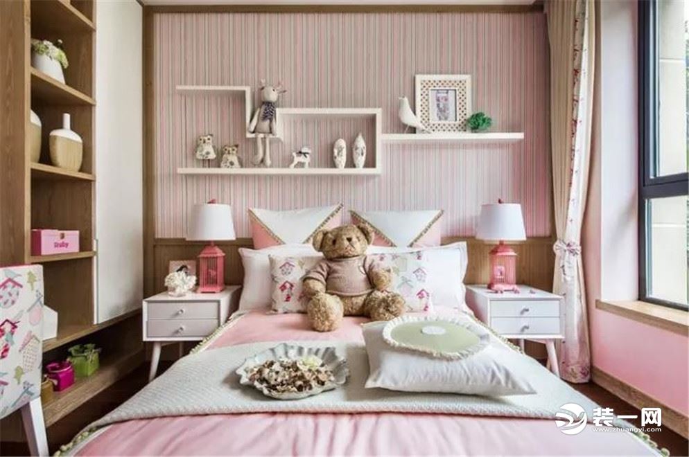 儿童房的床头贴着竖纹彩色壁纸，并装了个小搁架，摆着照片与可爱的摆饰，搭配上粉色调的床单。