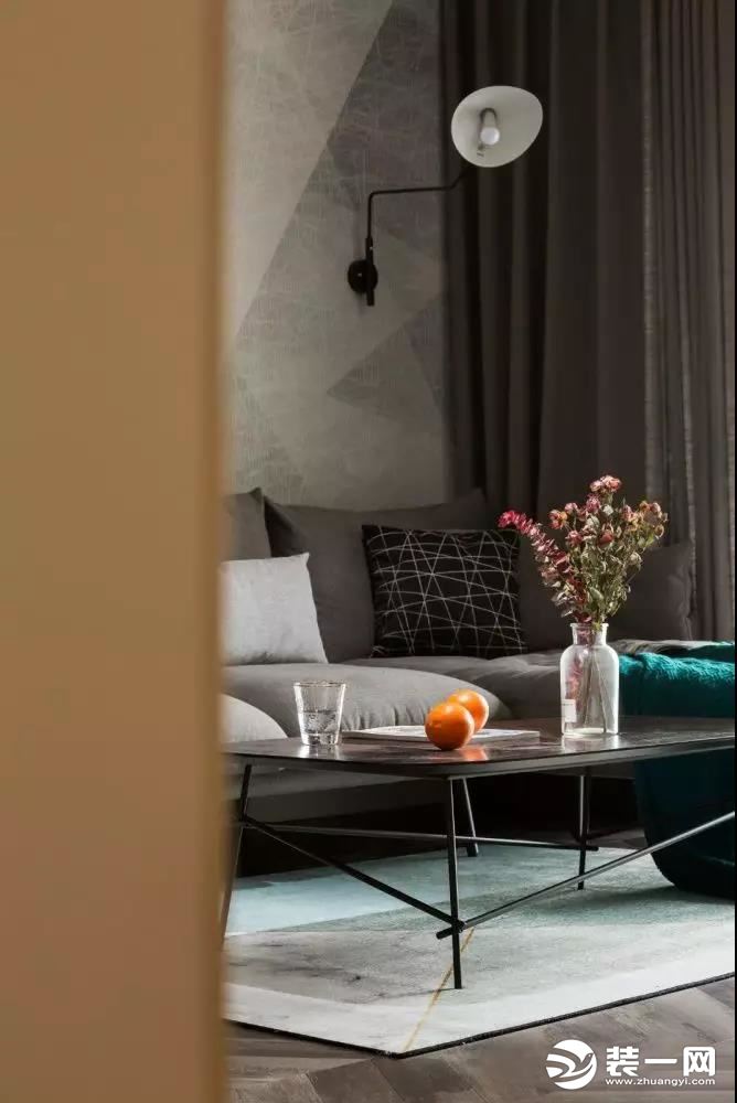 灰色布艺沙发简约而时尚，黑色茶几线条硬朗质感满满，搭毯的墨绿色与地毯色调相互呼应，辅以唯美浪漫的一抹