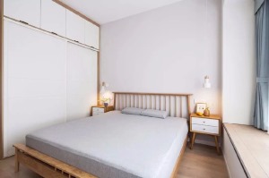 主卧室以白色和木色为主，搭配浅灰色的床品，营造出自然休闲的居住氛围。床两侧分别是大衣柜和飘窗榻榻米，