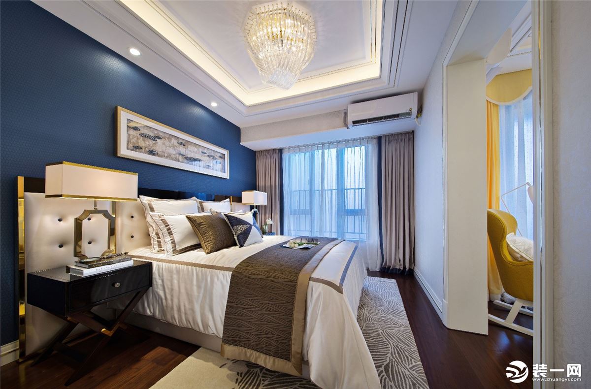卧室床头墙是一面深蓝色的背景，墙面上挂着横幅装饰画，搭配灰褐色的布艺床铺，让卧室显得静雅端庄而又时尚