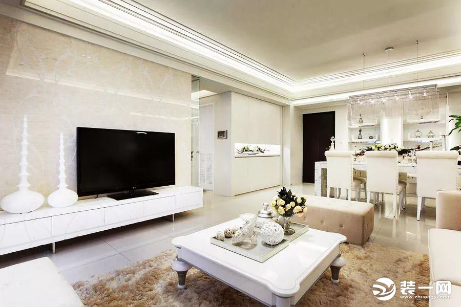 以米白色大理石作为电视主墙，搭配纯白色低矮电视柜和桌面装饰，给人干净利落的感觉