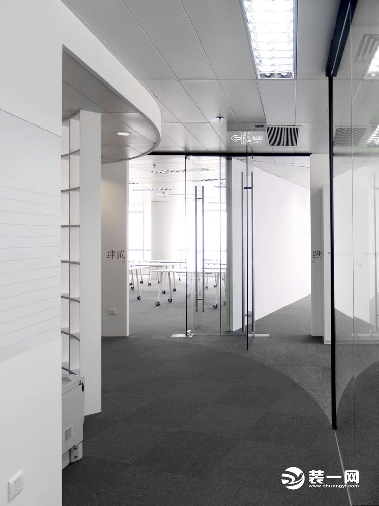 办公区的走廊过道设计比较符合现代简约风格，深色的地毯铺设、银灰色天花板装修及玻璃墙隔断。