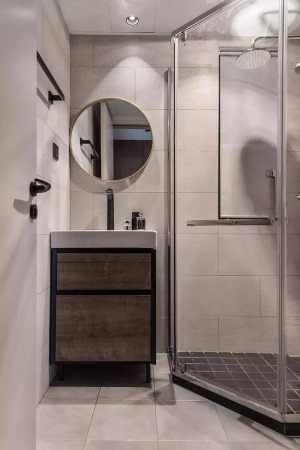 卫生间，钻石型的淋浴房以黑色小砖打底。浴室柜刚刚好安置在淋浴房旁的角落，挂一个圆形的装饰镜，细腻而精