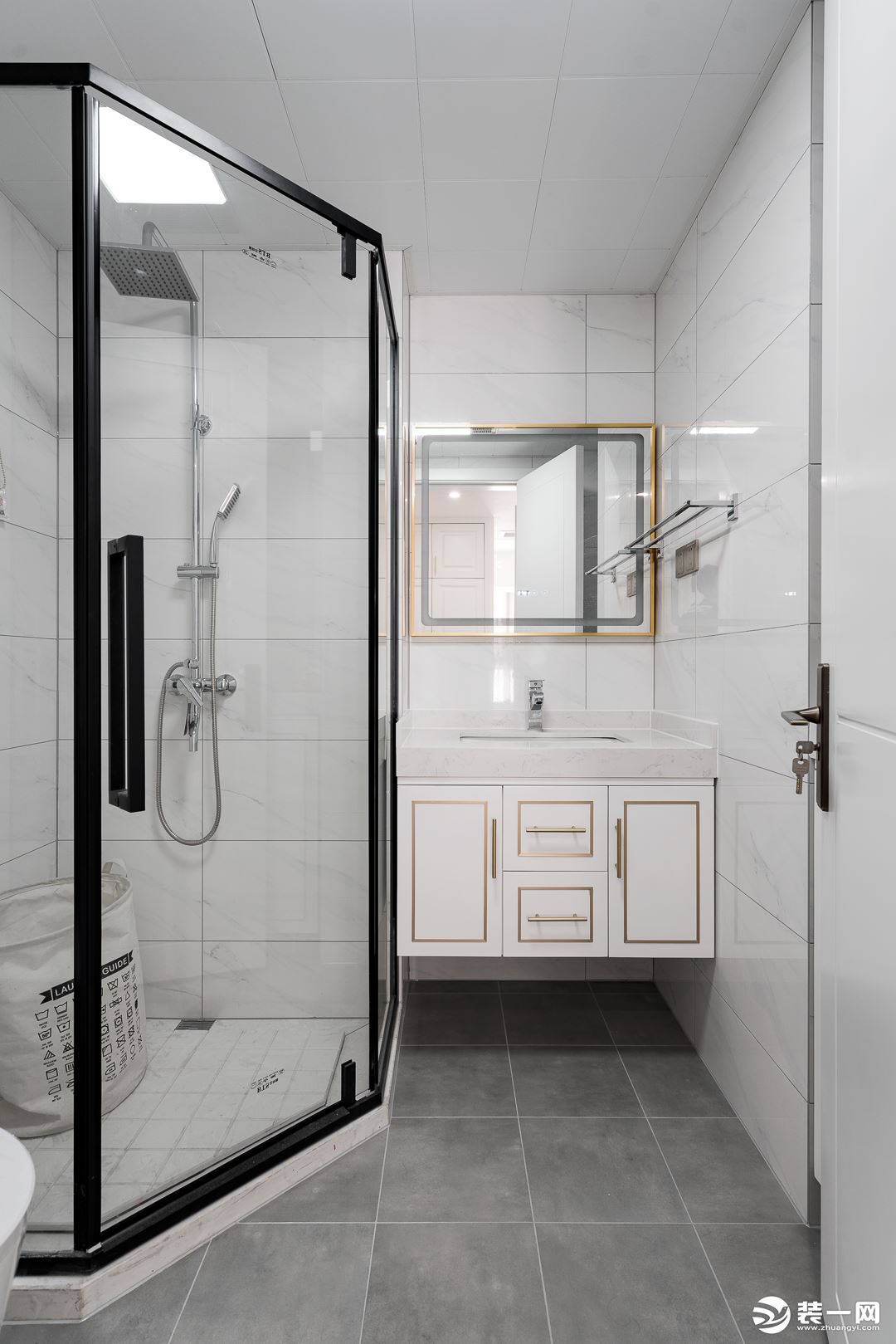 卫浴空间以白色瓷砖与花灰色地砖搭配，整体保持简单清爽的氛围。浴室柜的金边和淋浴房的黑框形成“黑金”。