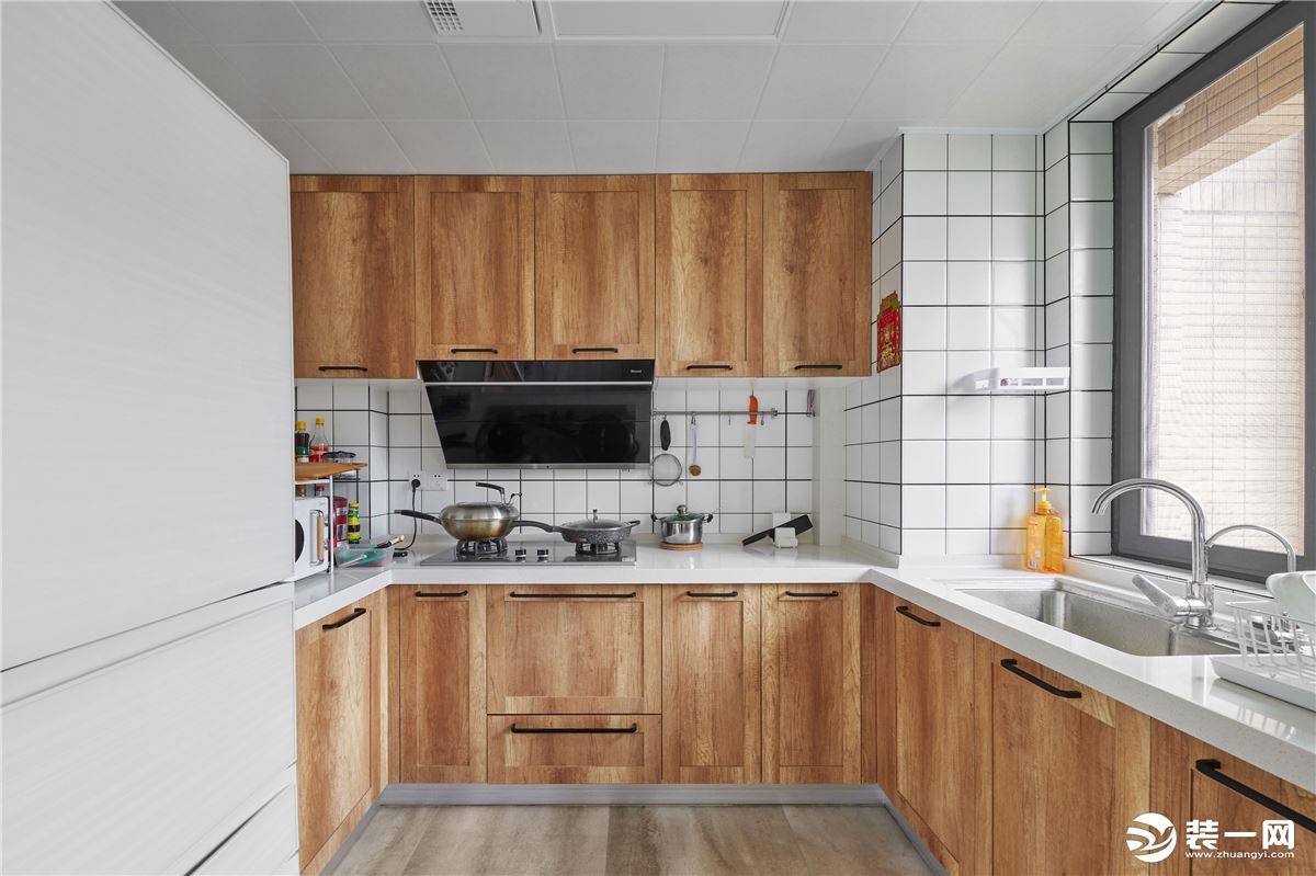  推开玻璃移门，是呈U型的厨房空间，动线合理流畅。淳朴质感的原木柜门搭配方格小白砖，清新文艺腔调十足