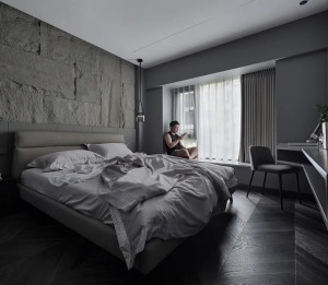 卧室床头墙以灰色岩石板材质打造，搭配深木色的木地板，灰色皮艺床与床单布置，天花以无主灯的吊平顶设计，
