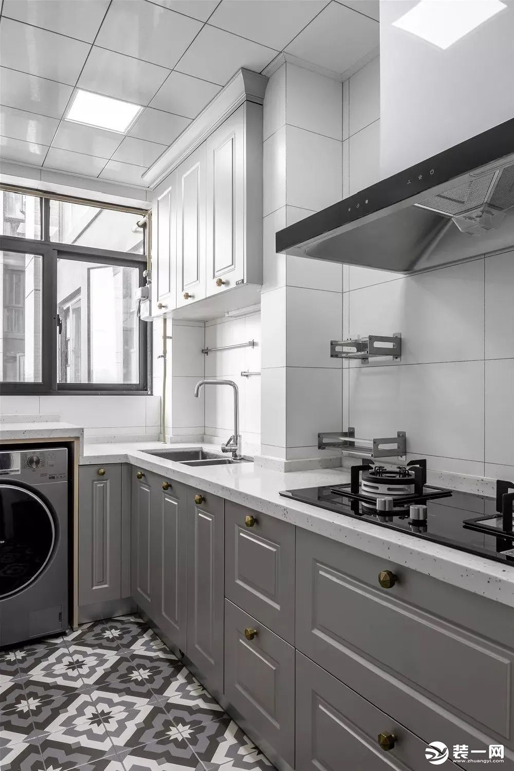 厨房空间做了L型橱柜设计，地面铺贴的灰白花砖，搭配灰色的橱柜门铜制金属拉手，看起来非常大气又有格调。
