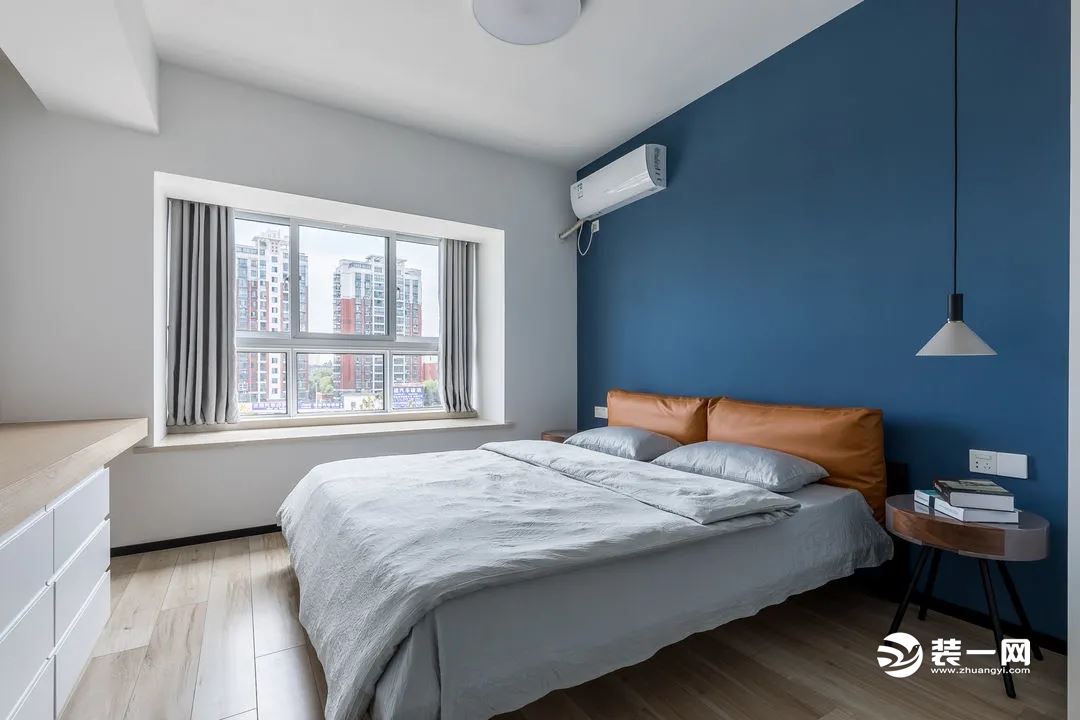 主卧，床头背景墙涂刷了蓝色的墙漆，加上了橙黄色的软包靠背，静谧且舒适却又带有一丝丝的活泼感。