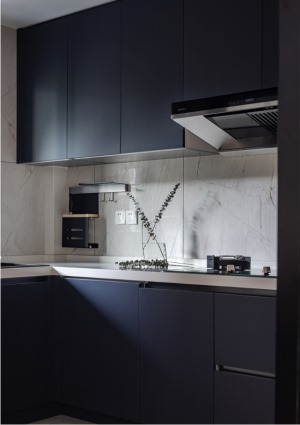 厨房定制了L型的橱柜，另一侧摆放冰箱，黑色橱柜与浅灰瓷砖的搭配，在光线的晕染下营造出一份静谧与雅致。